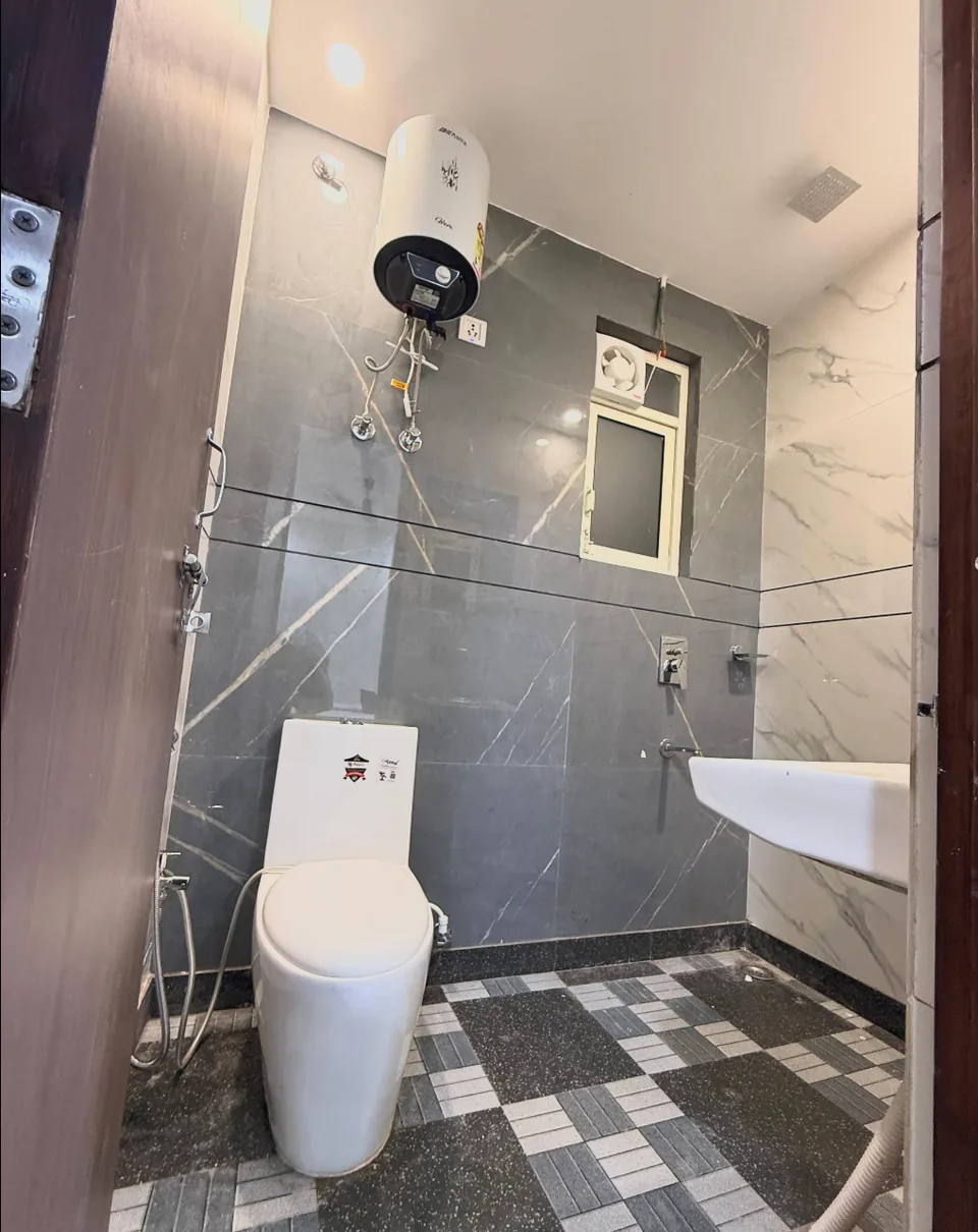 Tiled bathroom with a toilet, washbasin and wall-mounted electric geyser.