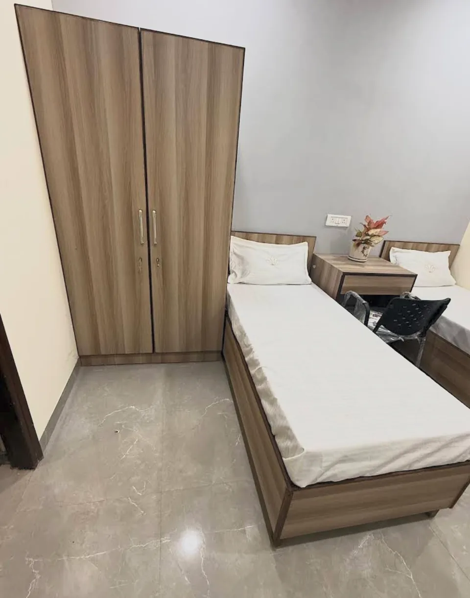 Twin-sharing room showing a full-height wooden almirah beside the beds.