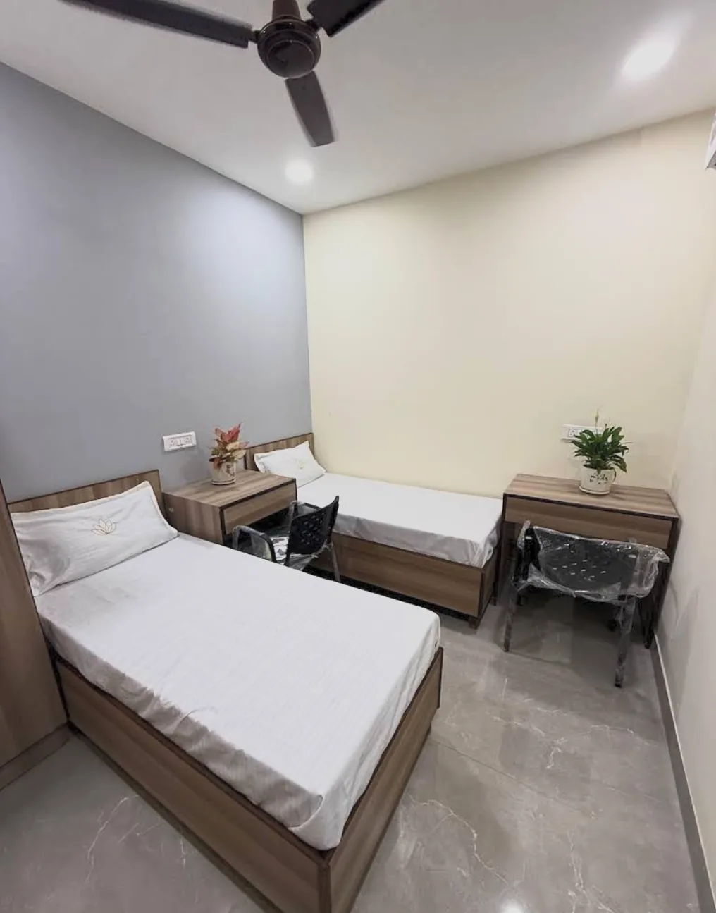 Twin-sharing room with two wooden beds, study desks, chairs and a ceiling fan.